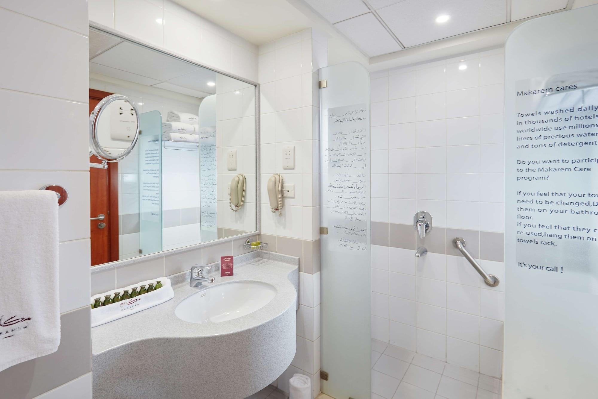 โรงแรมมากาเรม อุมม์ อัลกุรา Mecca ภายนอก รูปภาพ The photo shows a modern bathroom with a clean and minimalist design. There is a curved vanity sink with a large mirror above it, which also includes a circular mirror attached to the wall. The sink area has a few toiletries displayed. On one side, t