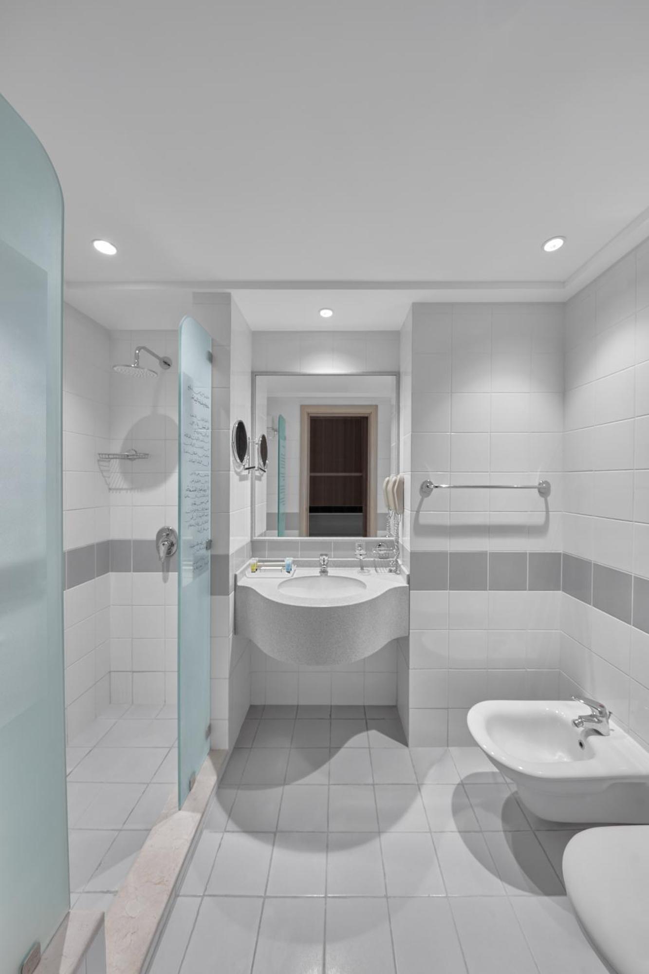 โรงแรมมากาเรม อุมม์ อัลกุรา Mecca ภายนอก รูปภาพ The photo shows a modern bathroom layout with a clean and minimalistic design. The walls are primarily covered in white tiles, with a horizontal band of gray tiles creating a stylish contrast. 

In the space, there is a round sink with modern fixture