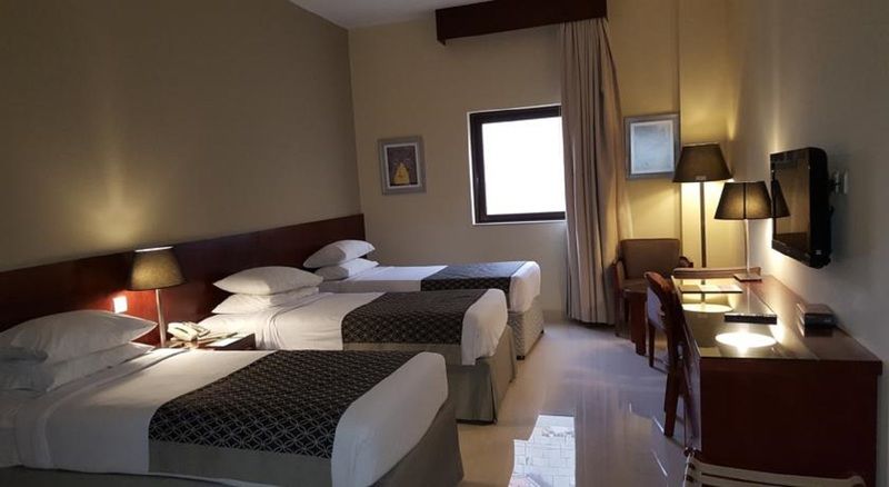 โรงแรมมากาเรม อุมม์ อัลกุรา Mecca ภายนอก รูปภาพ The photo shows a hotel room with two twin beds covered in white and patterned bedding. The walls are painted in a soft color, and there's a window with light-colored curtains. A small desk with a chair is positioned near the window, and there are tw