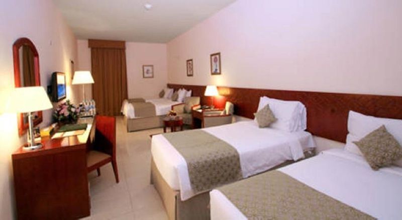 โรงแรมมากาเรม อุมม์ อัลกุรา Mecca ภายนอก รูปภาพ The photo shows a hotel room that features two sets of beds. The room is furnished with light-colored walls and a neutral color palette. Each bed has a light green and cream-colored bedspread. There’s a window with curtains, a desk with a chair, and 
