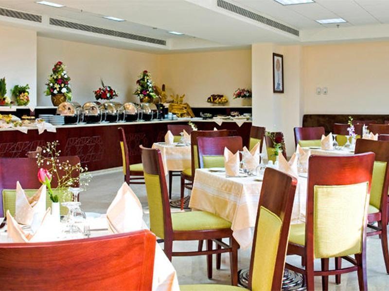 โรงแรมมากาเรม อุมม์ อัลกุรา Mecca ภายนอก รูปภาพ The photo depicts a dining area in a restaurant or banquet hall. There are several tables neatly arranged with light-colored tablecloths and stylish chairs featuring both wood and light green upholstery. Each table is set with utensils and decorative