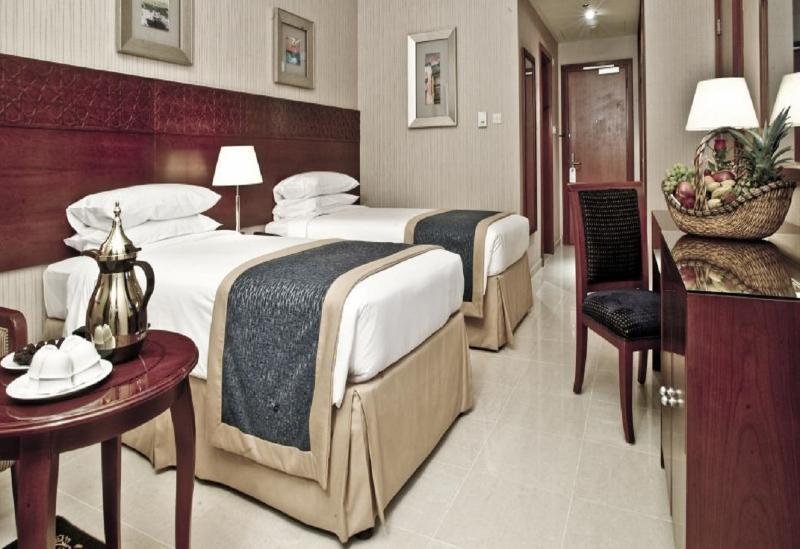 โรงแรมมากาเรม อุมม์ อัลกุรา Mecca ภายนอก รูปภาพ The photo shows a hotel room featuring two twin beds made with white linens and blue bed runners. A small bedside lamp is placed between the beds. On one side, there is a round table with a silver teapot and some small plates. To the right, there is 