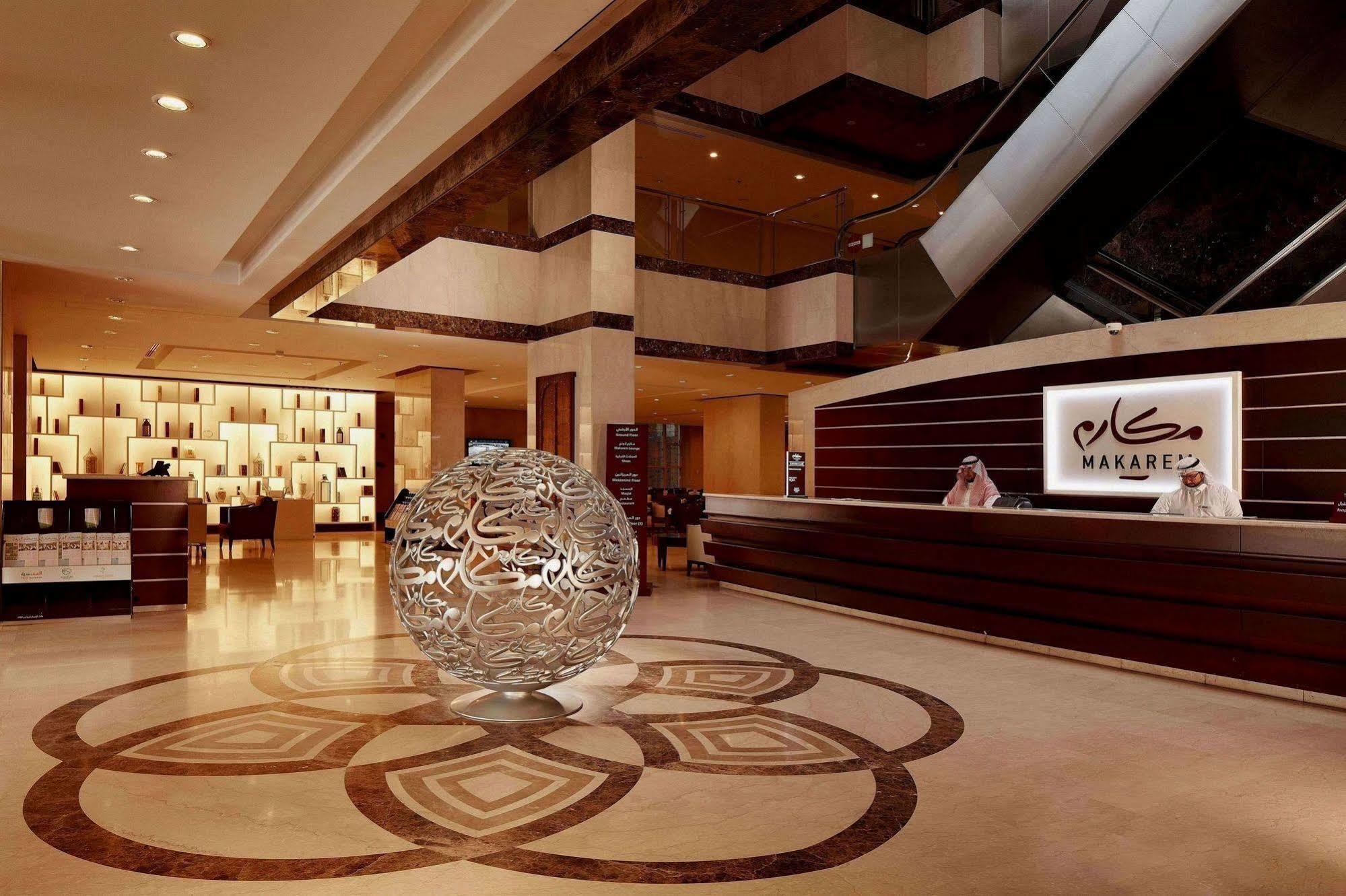 โรงแรมมากาเรม อุมม์ อัลกุรา Mecca ภายนอก รูปภาพ The photo shows an elegant hotel lobby featuring a modern and sophisticated design. In the center, there is a large decorative sphere with intricate patterns, placed on a stylized floor design. Behind the sphere, the reception desk is visible with st