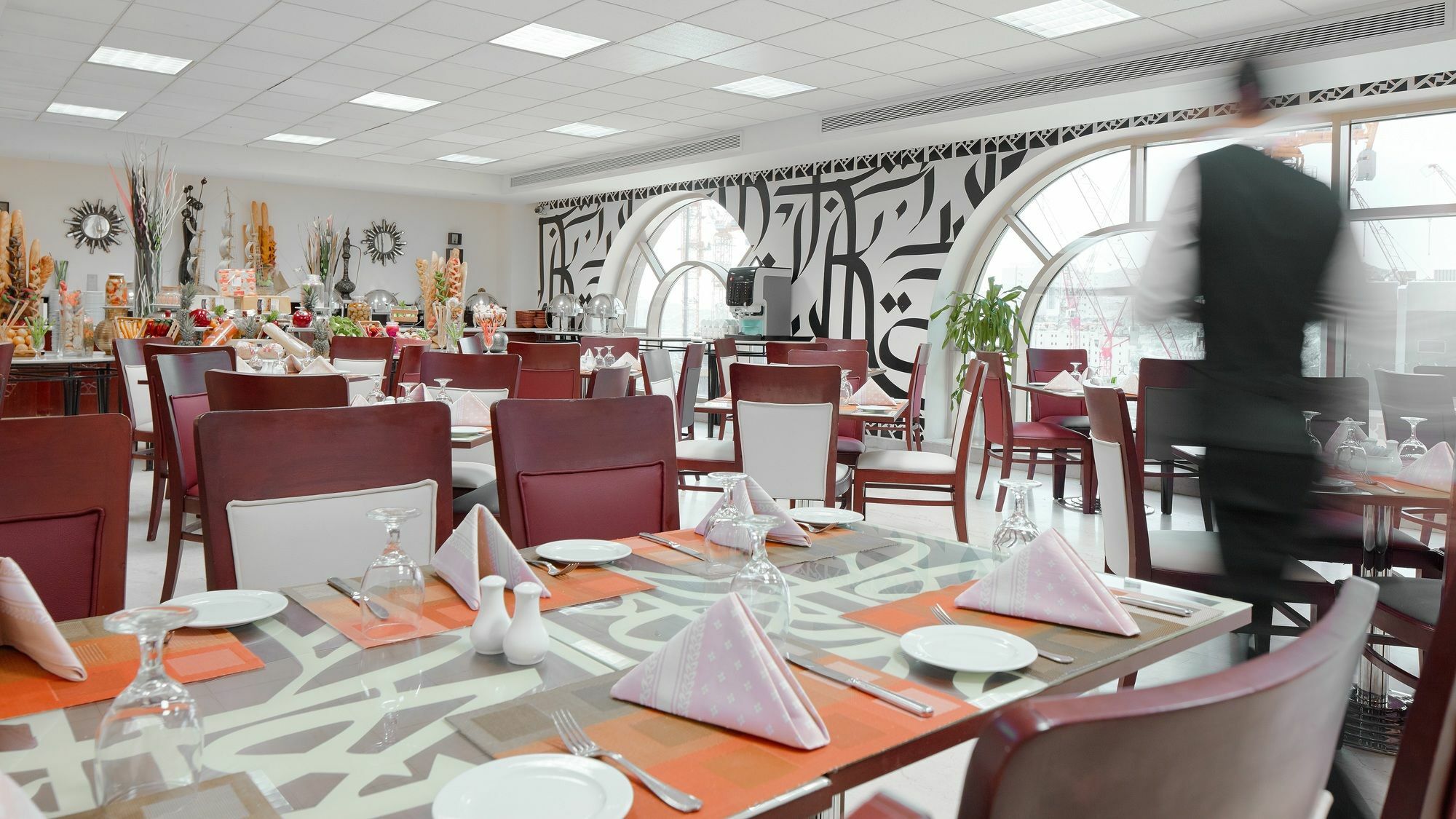 โรงแรมมากาเรม อุมม์ อัลกุรา Mecca ภายนอก รูปภาพ The photo shows the interior of a dining room in a restaurant. The space features modern decor with stylish furniture, including wooden tables and upholstered chairs. The tables are set with white plates, glassware, and neatly folded napkins in a tri